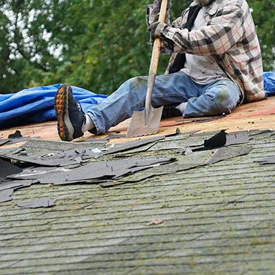 Worker removing old, moldy shingles from a residential roof with a shovel