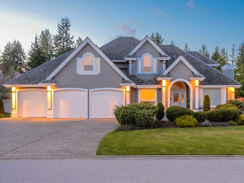 Front of a mid-class home with its front lights on while the sun sets